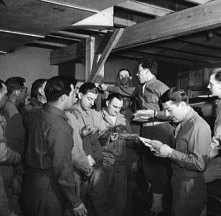 Servicemen crowded together reading letters at mail call