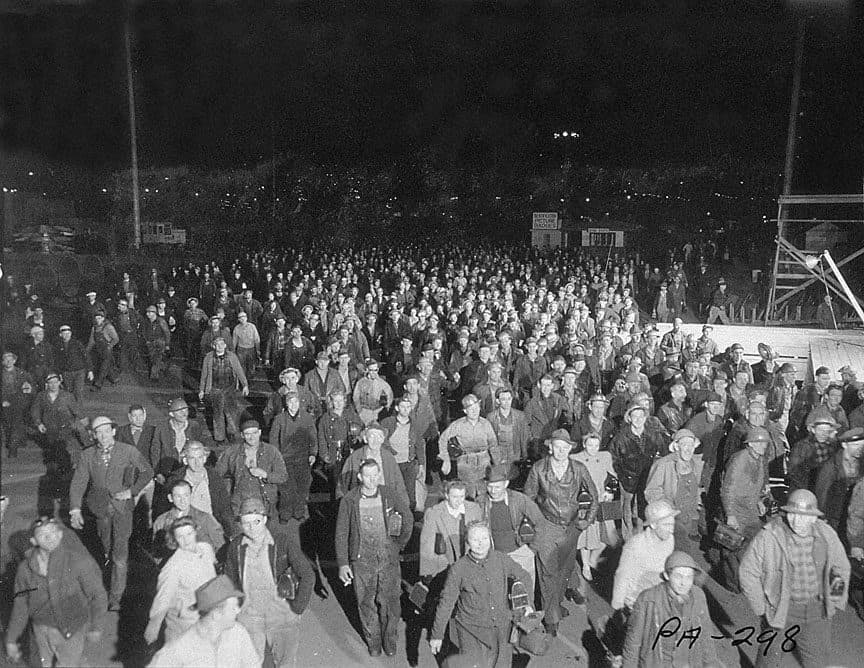 Hundreds of shipyard workers streaming out under floodlights at the end of a night shift, Portland