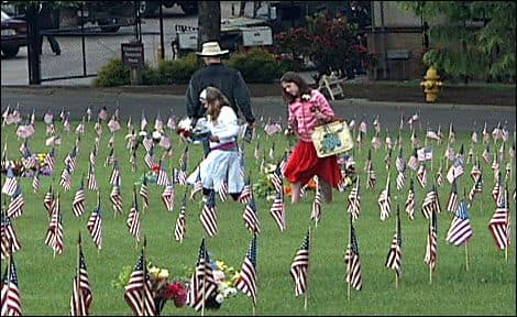 A family walking between rows of small American flags planted at Willamette National Cemetery