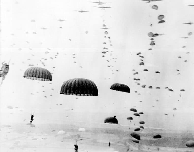 Paratroopers descending under open canopies, more aircraft above