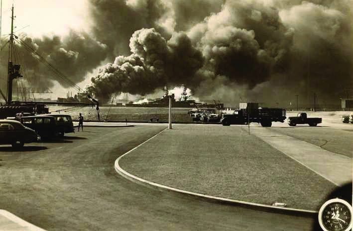 Cars stopped on a road as smoke rises in the distance during the attack on Pearl Harbor